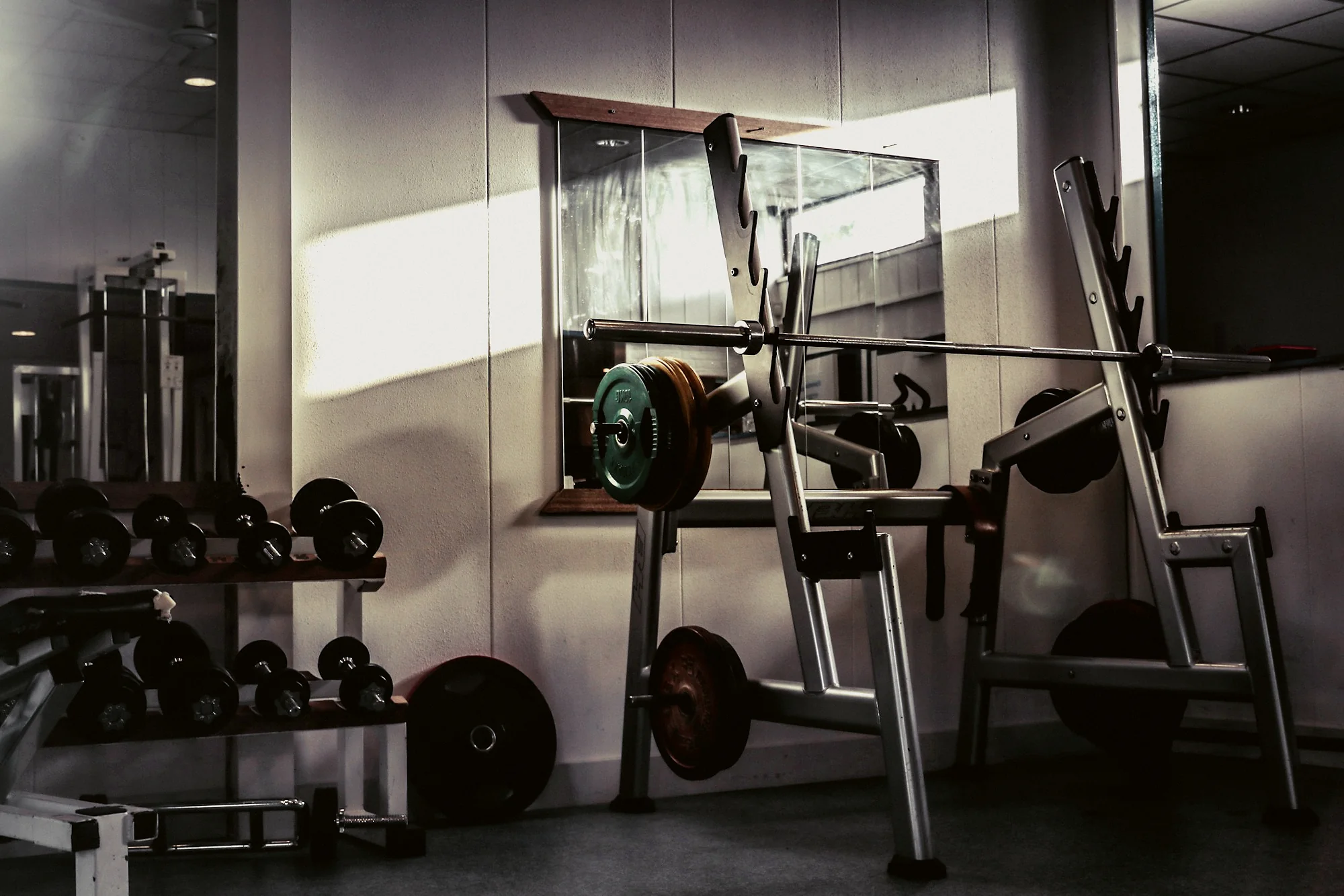 An empty weight room with a barbell, plates and side light from a window