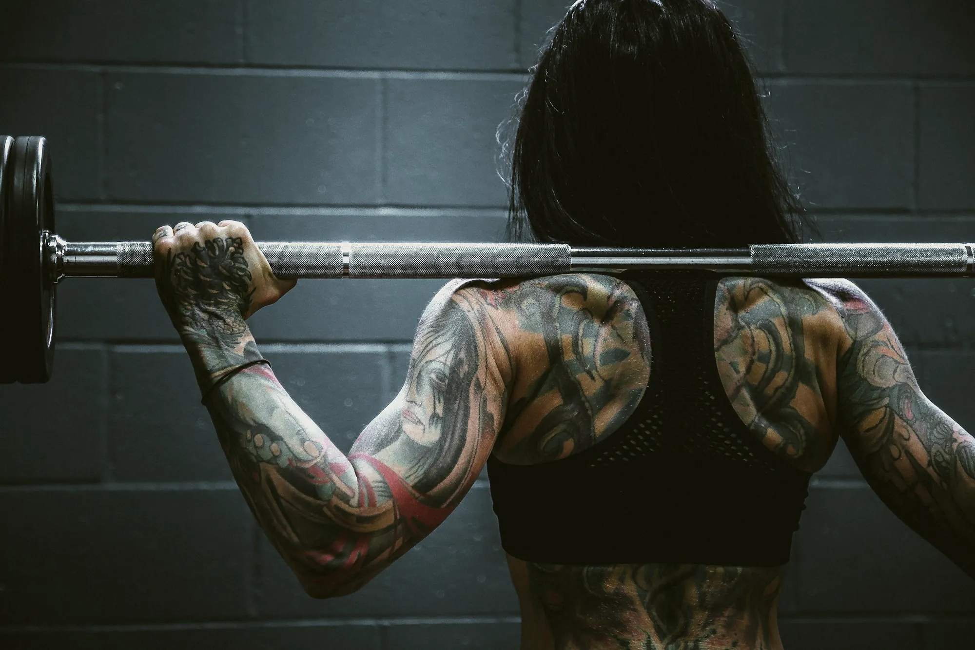 A woman seen from behind with a barbell across her shoulders, focused on her set