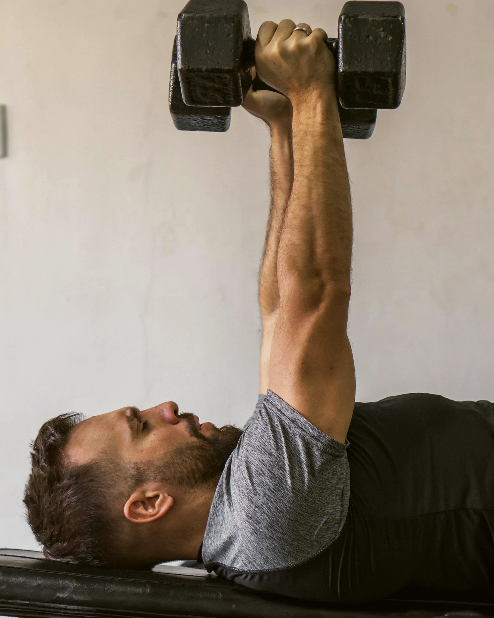 A man lying on a bench pressing dumbbells, eyes on the weight