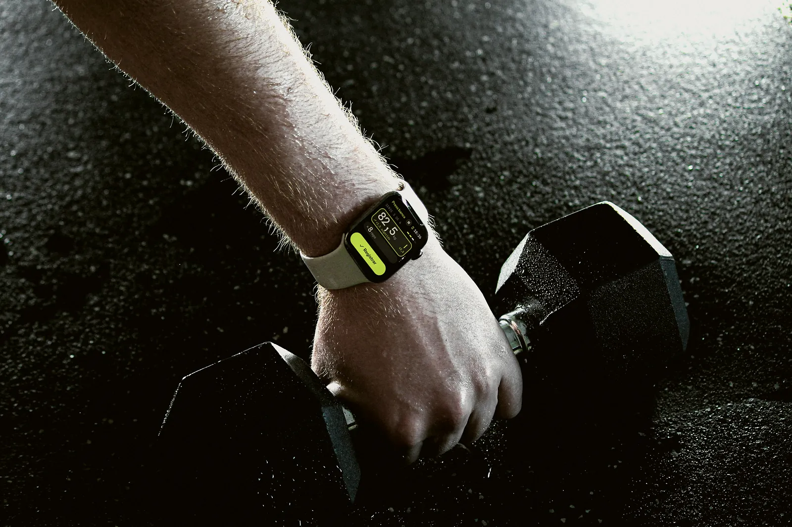 Composite of a wrist wearing an Apple Watch that shows Minthra: bench press at 82.5 kg, next to a dumbbell